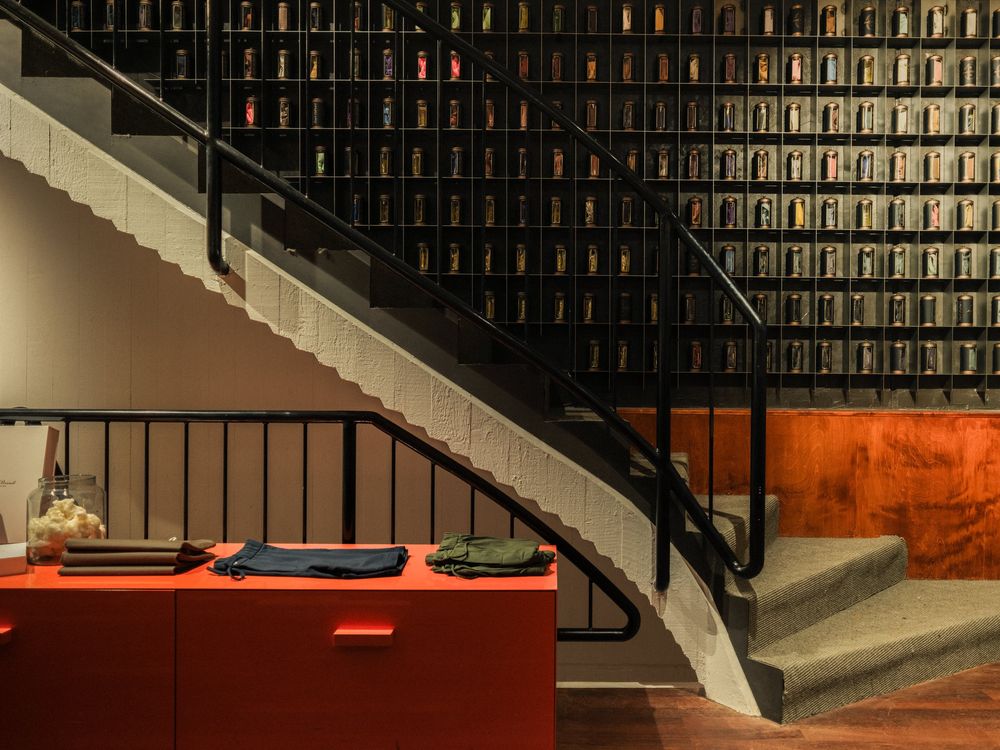 Geschwungene Treppe vor einer Wand aus Weinflaschen, davor ein roter Tisch