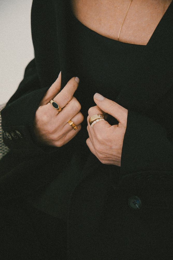 Hände mit Ringen halten einen schwarzen Mantel