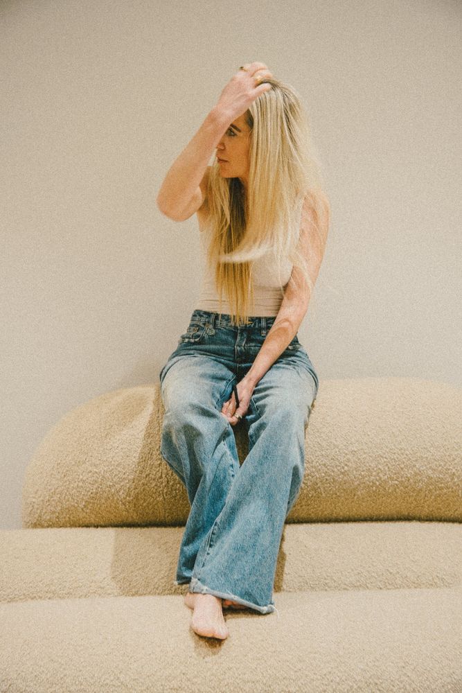 Frau in Jeans sitzt auf einem Sofa und greift ins Haar