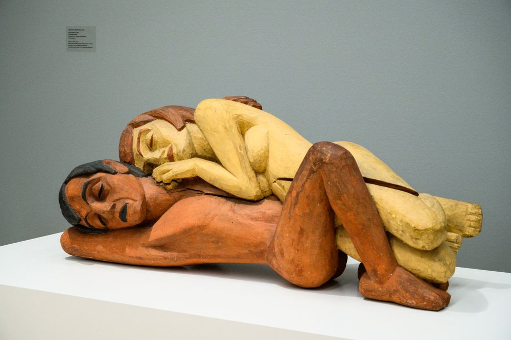 Liegende bemalte Holzskulptur auf einem Sockel