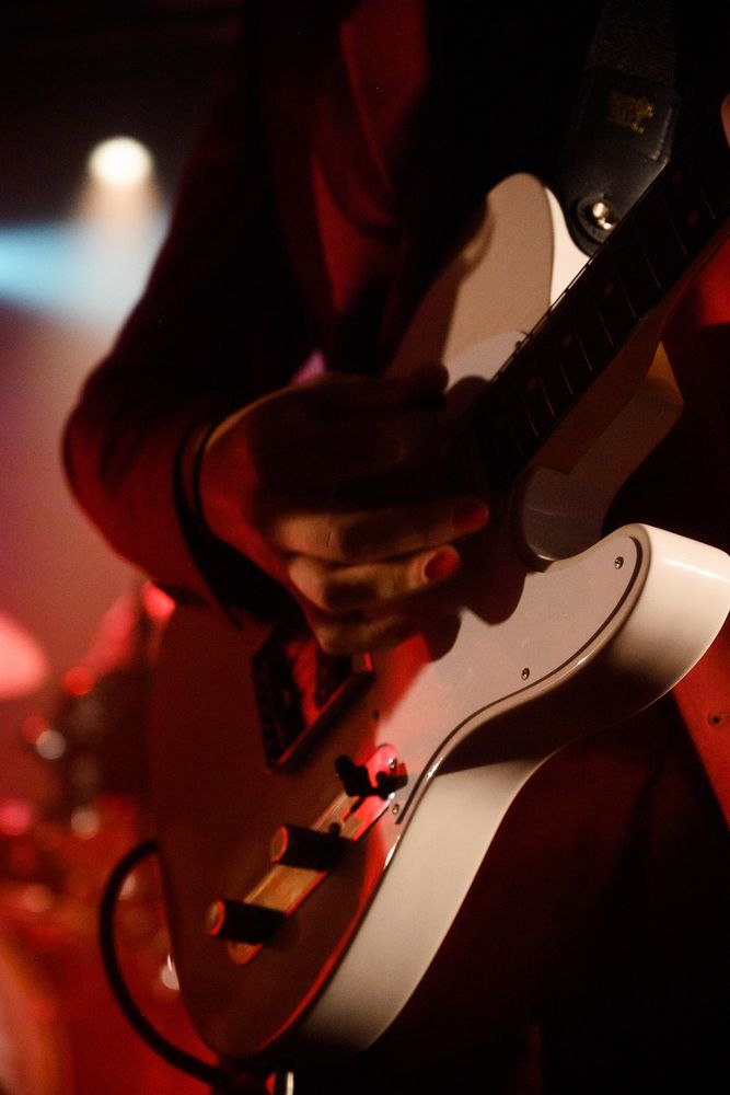 Hände an einer weissen Gitarre im roten Licht