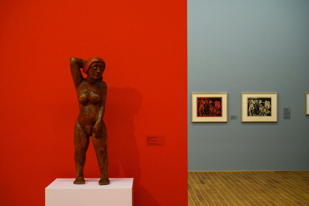 Stehende Holzfigur vor roter Wand mit Blick in den grauen Raum